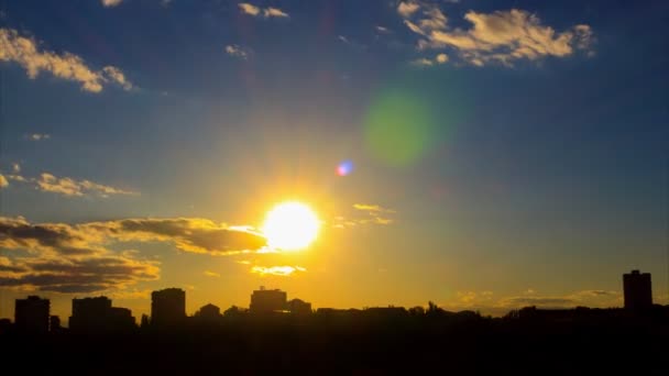 Lovely time lapse of sunset, with golden sun, with gray-white clouds, with azure sky, with lense flares, against the background of the city silhouette. The camera approach very fast — Stock Video