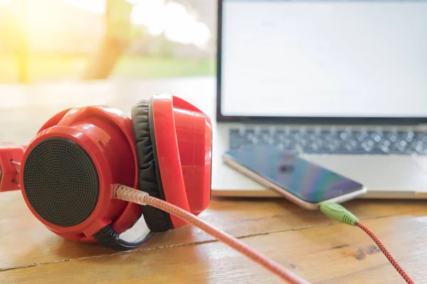 Red headphones, smartphone and laptop computer on wooded table — Stock Photo, Image