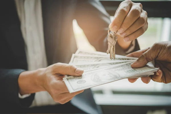 Manos del agente inmobiliario dando llaves al cliente y billete de banco — Foto de Stock