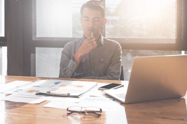 Genç Asyalı adam dizüstü bilgisayar ve belgenin çalışma performansı ve ofis, finansal yatırım kavramı düşüncesinde analiz eder