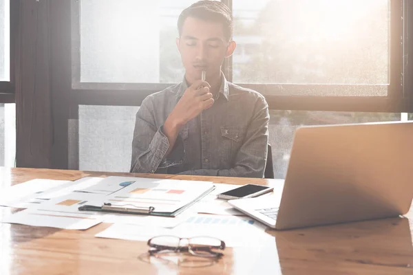 Joven hombre asiático que trabaja con ordenador portátil y documento mientras analiza el rendimiento y el pensamiento en la oficina, concepto de inversión financiera —  Fotos de Stock