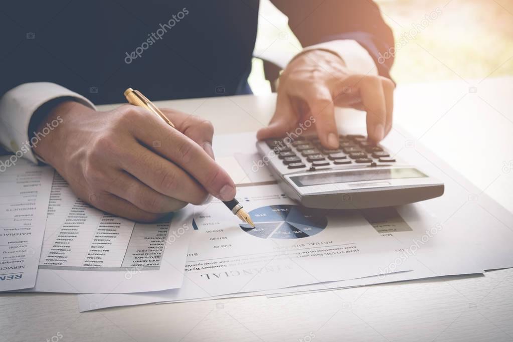 Businessman pen pointing graph chart while using a calculator to calculate the numbers. Accounting , Accountancy, Calculation Concept. vintage filter effect