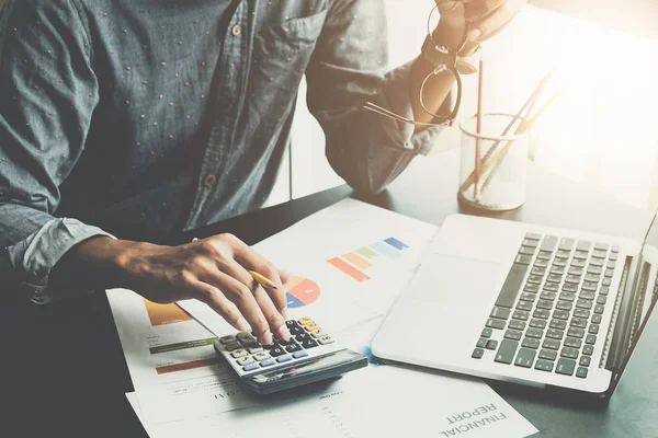 Um homem que trabalha sobre financeira e análise documento de negócios com calculadora e segurando óculos em seu escritório para calcular despesas, Contabilidade conceito — Fotografia de Stock