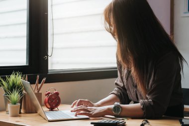 İş kadını, ofisteki ahşap masada matematik finansmanı için dizüstü bilgisayar ve hesap makinesi kullanıyor. 
