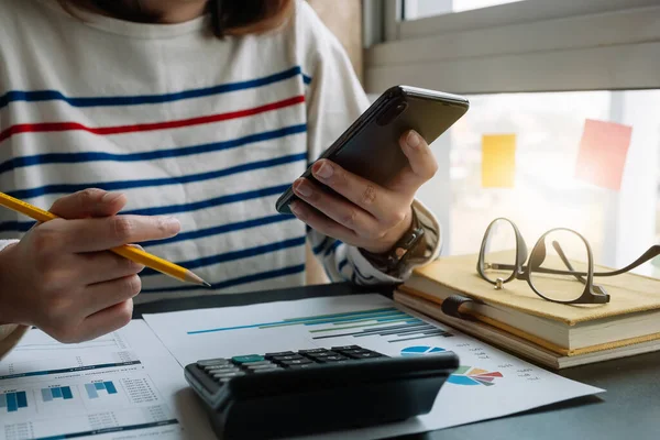 Fechar o contador mão segurando smartphone enquanto trabalhava na calculadora para calcular o relatório de dados financeiros , — Fotografia de Stock