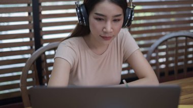 Masada oturan genç bir kız öğrenci, evde çalışırken dizüstü bilgisayar kullanıyor.