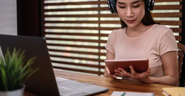 Een Aziatische vrouwelijke student zit aan tafel, met behulp van tablet bij het studeren online thuis — Stockfoto