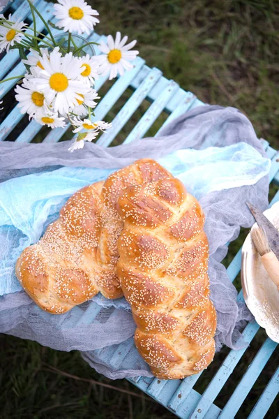 Newly-baked wheat long loaf outdoors. Jewish challah. Long loaf a braid with sesame on a blue wooden table on the street.