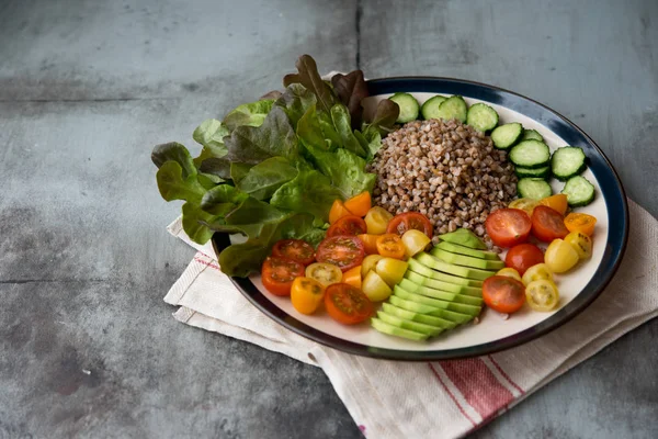 Healthy food. A plate with boiled buckwheat, tomatoes, avocado and a cucumber. Food and health.