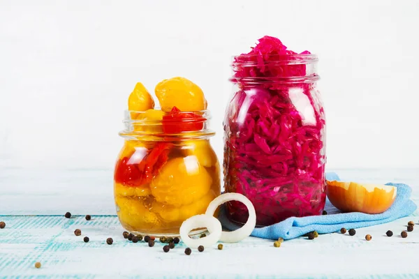 Two jars of different fermented vegetables stand on a wooden table in the center of the frame. Pickled red cabbage and pickled squash. Horizontal orientation.