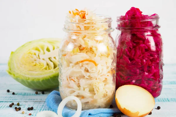 Two cans of different colored fermented cabbage stand on a wooden table in the center of the frame around fresh cabbage, onions and spices. Sauerkraut red cabbage and sauerkraut white cabbage close. Horizontal orientation. — Stock Image Two Cans Different Colored Fermented Cabbage Stand Wooden Table Center Royalty Free Stock Images