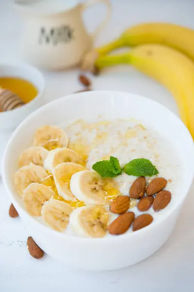 Oatmeal with honey, banana and nuts in a plate on a white background.