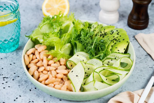 Vegetarian green salad bowl with fresh vegetables and canned white beans on a gray concrete background. Horizontal photo.