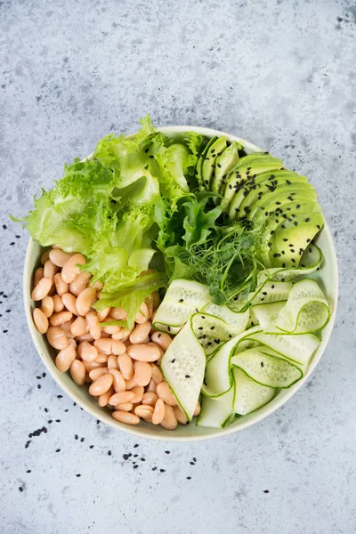 Vegetarian green salad bowl with fresh vegetables and canned white beans on a gray concrete background. Vertical photo. Top view.