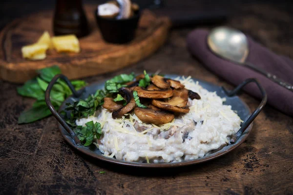 Italian dish risotto with mushrooms, Parmesan and herbs. Risotto in a copper plate on a wooden brown background. Selective focus