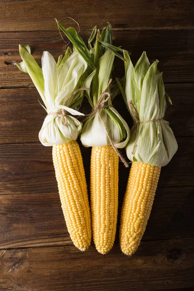Granos de maíz maduro sobre fondo de madera. mazorca de maíz y hojas verdes sobre fondo de madera, alimentos Top viev, Copyspace — Foto de Stock