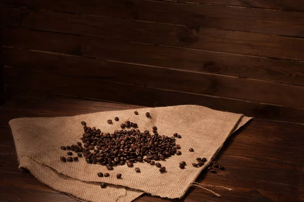 Coffee beans on sacking and wooden background — Stock Photo, Image