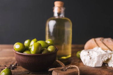 Yeşil Zeytin, ciabatta, ahşap bir tahta üzerinde beyaz peynir dilimlenmiş. Bir cam şişe zeytinyağı. Peynir beyaz. Ciabatta. Siyah bir zemin üzerine zeytin