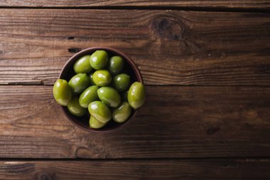 Green olives in a ceramic bowl on a wooden background. Background of olives. Background with green olives. Olives. Copyspace. Green olives and branch of bay leaf clipart