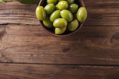 Yeşil zeytin ahşap arka plan üzerinde bir seramik kase. Zeytin arka plan. Yeşil Zeytin ile arka plan. Zeytin. Boşaltmak. Yeşil Zeytin ve defne yaprağı Şubesi