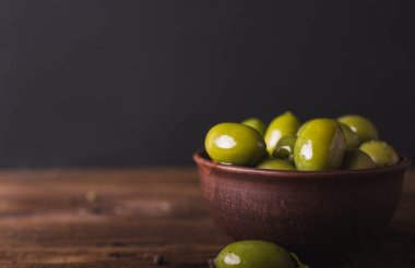 Bir ahşap tahta üzerinde yeşil zeytin, defne yaprağı. Zeytin siyah bir arka plan. Boşaltmak