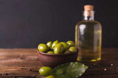 Bir ahşap tahta üzerinde yeşil zeytin, defne yaprağı. Zeytin siyah bir arka plan. Boşaltmak