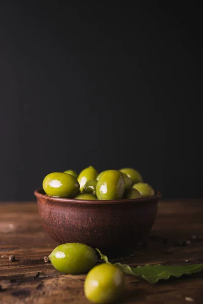 Зеленые оливки, лавровый лист на деревянной доске. Оливки на черном фоне . — стоковое фото