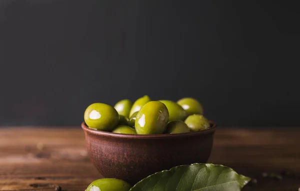 Зеленые оливки, лавровый лист на деревянной доске. Оливки на черном фоне . — стоковое фото