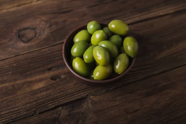 Green olives in a ceramic bowl on a wooden background. Background of olives. Background with green olives. Olives. Copyspace. Green olives and branch of bay leaf