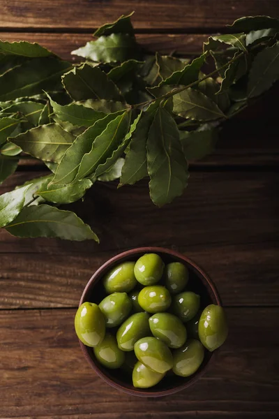 Green olives in a ceramic bowl on a wooden background. Background of olives. Background with green olives. Olives. Copyspace. Green olives and branch of bay leaf