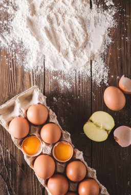 Paket ahşap arka plan üzerinde kırık yumurta ve yumurta. Un üzerinde ahşap bir masa dağıldı. Yumurta kabuğu. Fotoğraf kavramı pişirme 