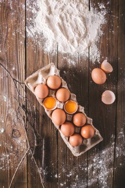 Paket ahşap arka plan üzerinde kırık yumurta ve yumurta. Un üzerinde ahşap bir masa dağıldı. Yumurta kabuğu. Fotoğraf kavramı pişirme 