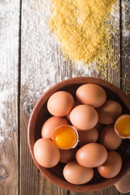 Kahverengi yumurta ve ahşap masa üzerinde kahverengi bir seramik kase kırık yumurta. Rustik tarzı. Yumurta. Un üzerinde ahşap bir masa dağıldı. Fotoğraf kavramı pişirme. Erişte, makarna. yumurta makarna