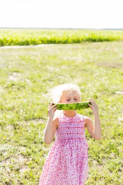 Bir sarışın küçük kız bir karpuz dilimi elinde tutar. Kız bir karpuz yiyor