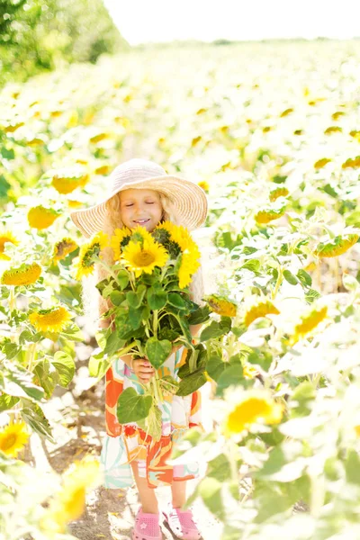 Ayçiçeği tarlası kıvırcık beyaz saçlı küçük kız. Kız bir hasır şapka ve sarafan