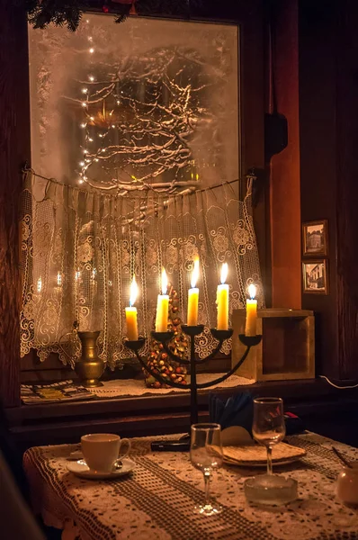 Five candles burning in menorah on a table on foreground and frosted window with snowed tree outside — Stock Photo, Image