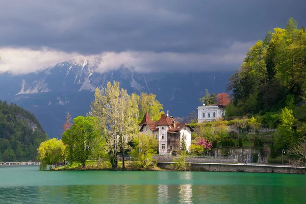 Vista panorámica del lago Bled con muelle bajo la luz del sol y montañas cubiertas de nubes en el fondo en primavera, Eslovenia — Foto de Stock