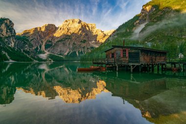 Lago di Braies 'in (Pragser Wildsee) ahşap kulübesi, güneşli tekneleri ve dağları, pürüzsüz göl suyu, Güney Tyrol, Dolomitler, İtalya