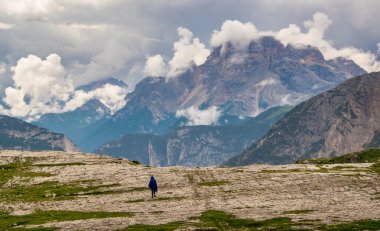 Bulutlarla kaplı dağ zirvelerinin muhteşem manzarası. Ön planda mavi pançolu bir turist figürü. Tre Cime di Lavaredo Ulusal Parkı, Dolomites, İtalya 'da Unesco Dünya Mirası