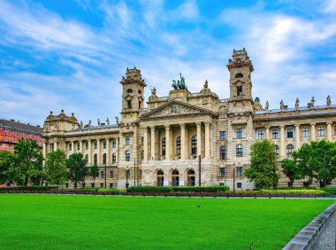 Macaristan, Budapeşte 'deki ünlü parlamento binasının karşısındaki eski Adalet Bakanlığı' nın muhteşem binası. Ön planda yeşil çimenler var. Resimli gökyüzü