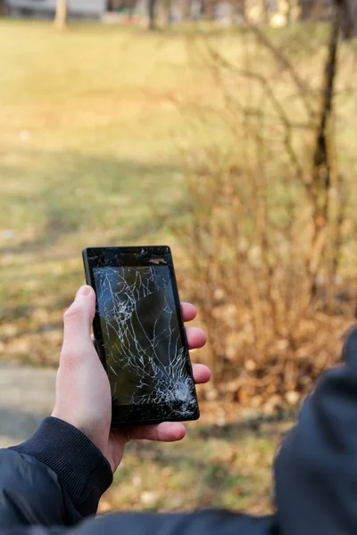 Human hand holding smart phone broken cracked damaged screen