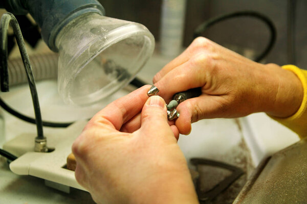 Hands of dental technician processing metal oral prosthesis