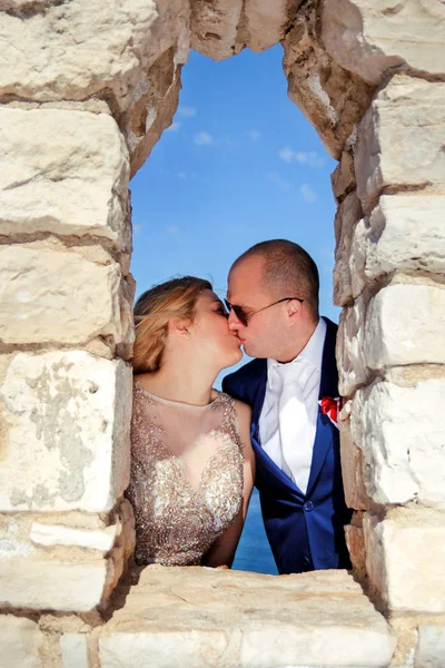 Pareja casada de pie y besándose en la ventana de la pared de piedra —  Fotos de Stock
