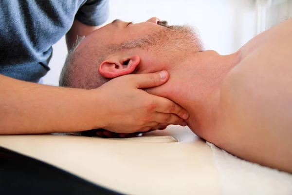 Мужчина, принимающий массаж мышц шеи за массажным столом — стоковое фото