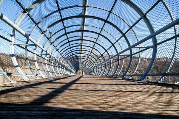 Modern architecture. Bridge overpass with circular steel construction. Half-through warren truss footbridge. Detail of a pedestrian suspension wooden and steel footbridge. — Stock Photo, Image