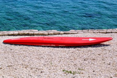 Denizin kenarında sahilde dalgalar üzerinde kırmızı bir sörf tahtası. Kum üzerinde surfboard ile plaj manzara. Beyaz kumlu plajda sörf tahtası. Sörf tahtası sahilde güneşte eğlence bekliyor.