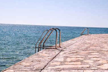 Deniz plajda Yüzme Küpeşte. Çelik Küpeşte, yüzme, mavi deniz, sahil, dalgalar, yaz, seyahat, doğal çevre, Akdeniz, Adriyatik Denizi. Küpeşte ile deniz girişine.