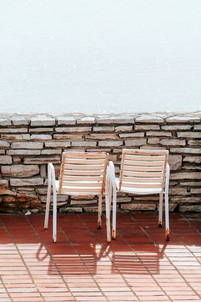 Bílá židle na balkoně. Tradiční středomořské přímořské a doby odpočinku na terase bílé staré židle a úžasné modré moře. Prázdné židle se dívají směrem k moři, obklopený kamennou zdí. — Stock fotografie
