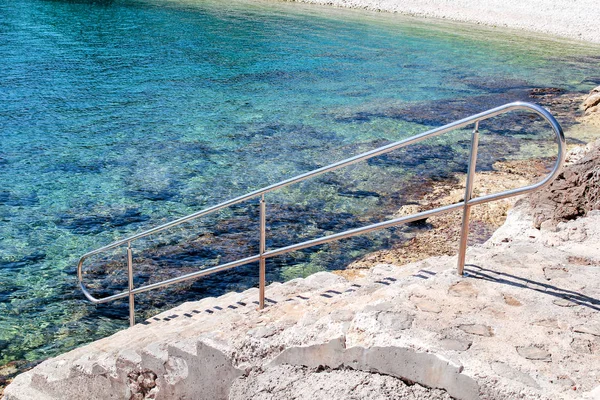 Corrimano nuoto sulla spiaggia del mare. Corrimano in acciaio, nuoto, mare blu, mare, onde, estate, viaggi, ambiente naturale, Mediterraneo, mare Adriatico. L'ingresso al mare con corrimano . — Foto Stock