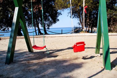 Plajda denizin kenarında kırmızı sallanır. Boş zinciri içinde çocuk oyun alanı, güneşli gün, yaz saati sallanır. Turizm, seyahat, yüzme, mavi deniz, doğal çevre, Akdeniz, Adriyatik Denizi.